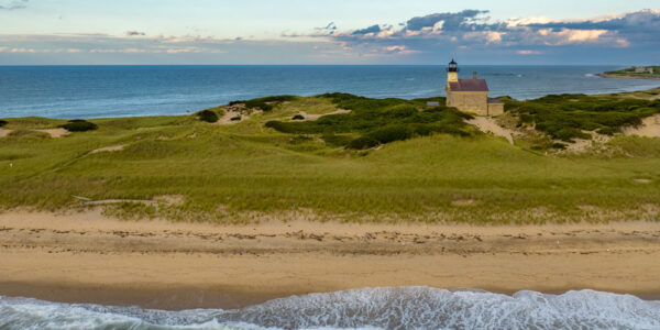 Aerial view of a lighthouse surrounded by grassy dunes overlooking the ocean on Block Island